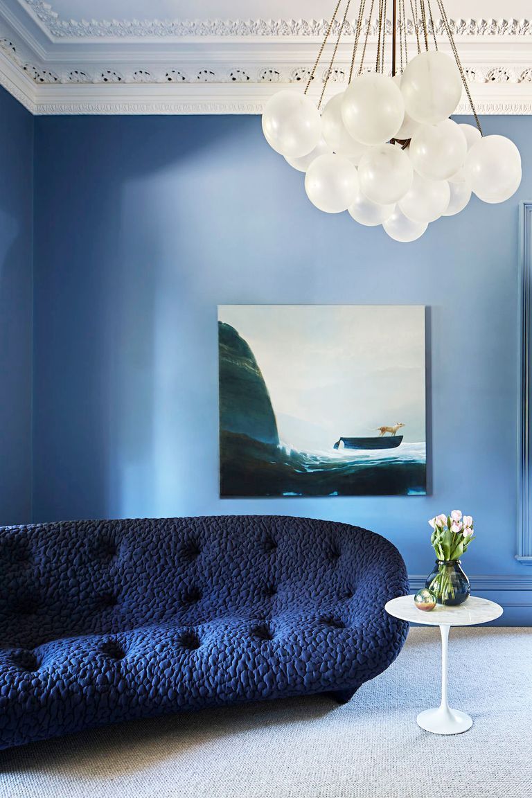 Blue living room with a curved, textured sofa, a seascape painting, and a spherical chandelier.