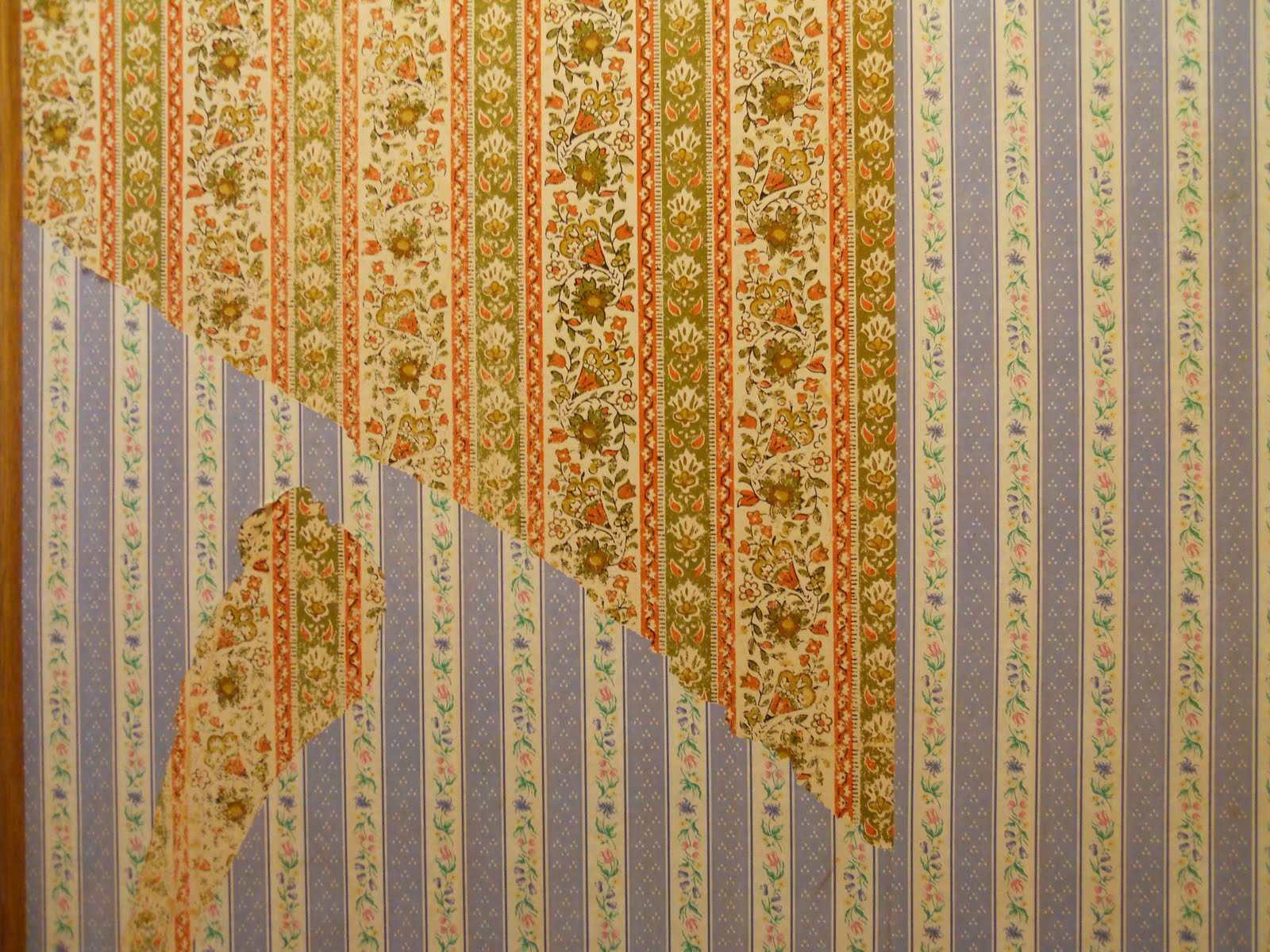 Wallpaper being removed, showing floral and striped patterns on the wall.
