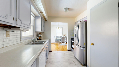 Kitchen with white cabinets, stainless steel refrigerator, and view into dining room with hardwood floors.