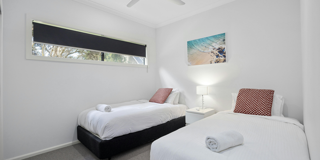 Two twin beds in a bright room with a window, artwork, and a nightstand between them.