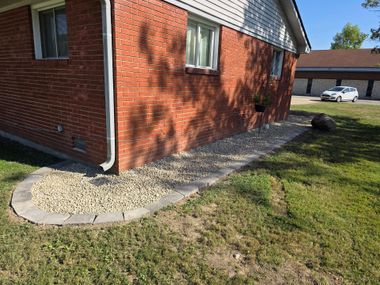 Brick house corner with gravel border and grassy yard beside a sidewalk
