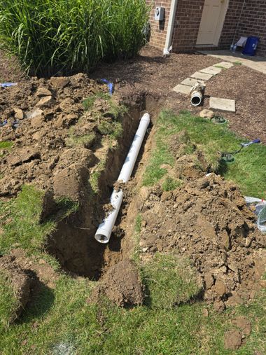 Backyard trench with a white pipe laid in dirt beside a house and lawn