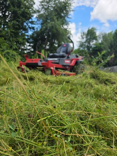 Red lawn mower cutting tall grass in a green field under a blue sky