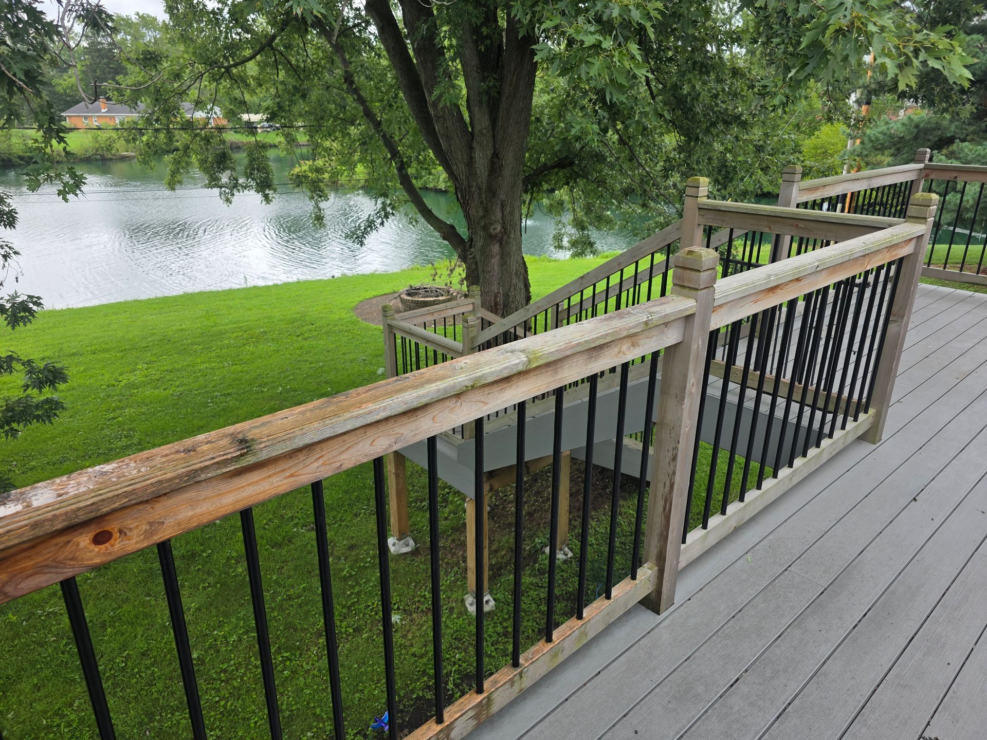 Wooden deck railing overlooking a grassy lakeside with trees and calm water