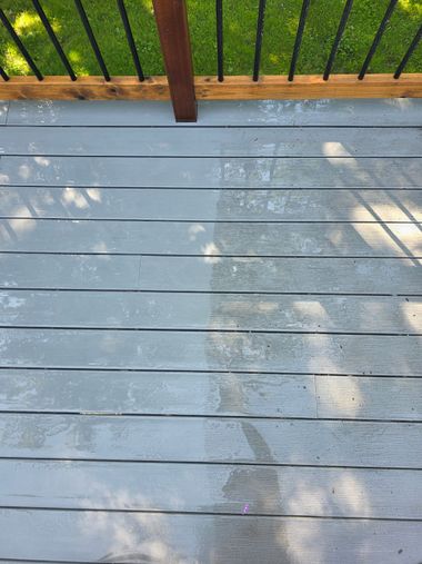 Sunlit gray deck boards beside a black railing and patch of green grass shadows