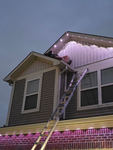 Ladder leaning to roof on a house with purple string lights at dusk