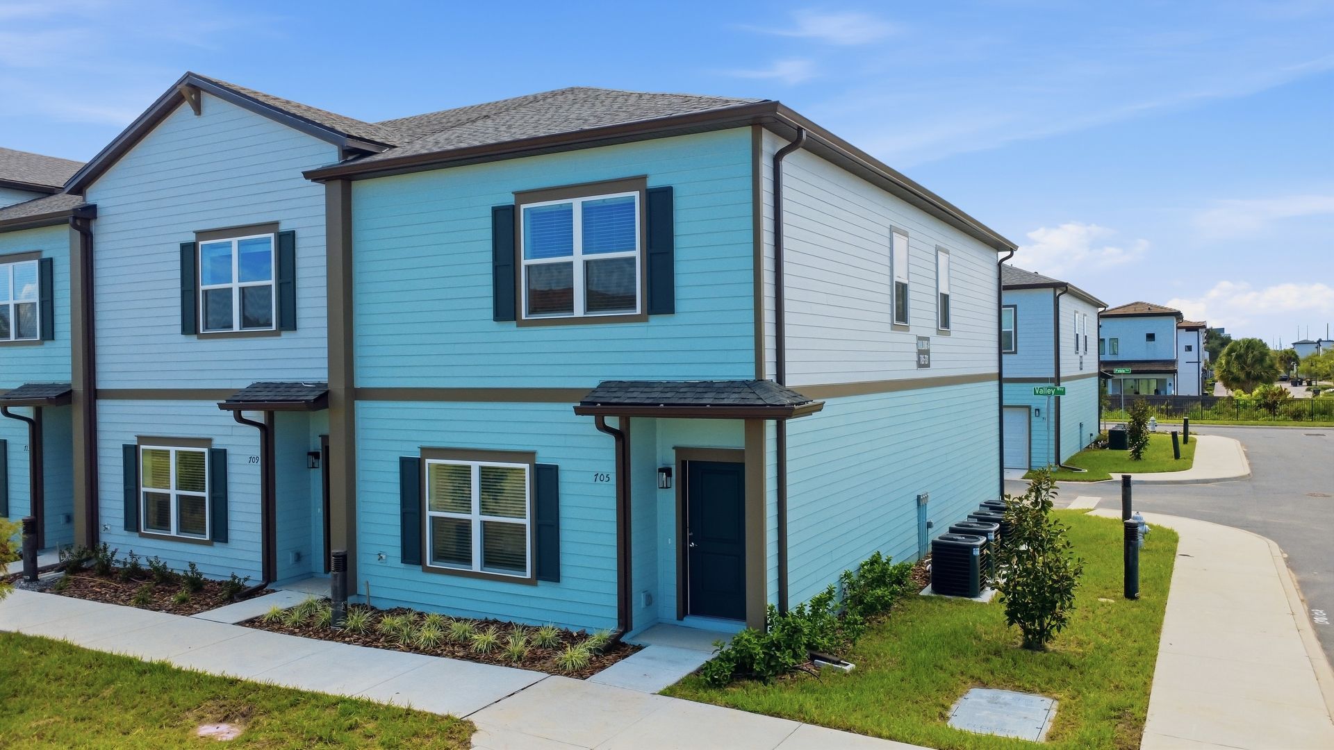Row of modern blue townhouses with white trim along a paved sidewalk under a clear sky