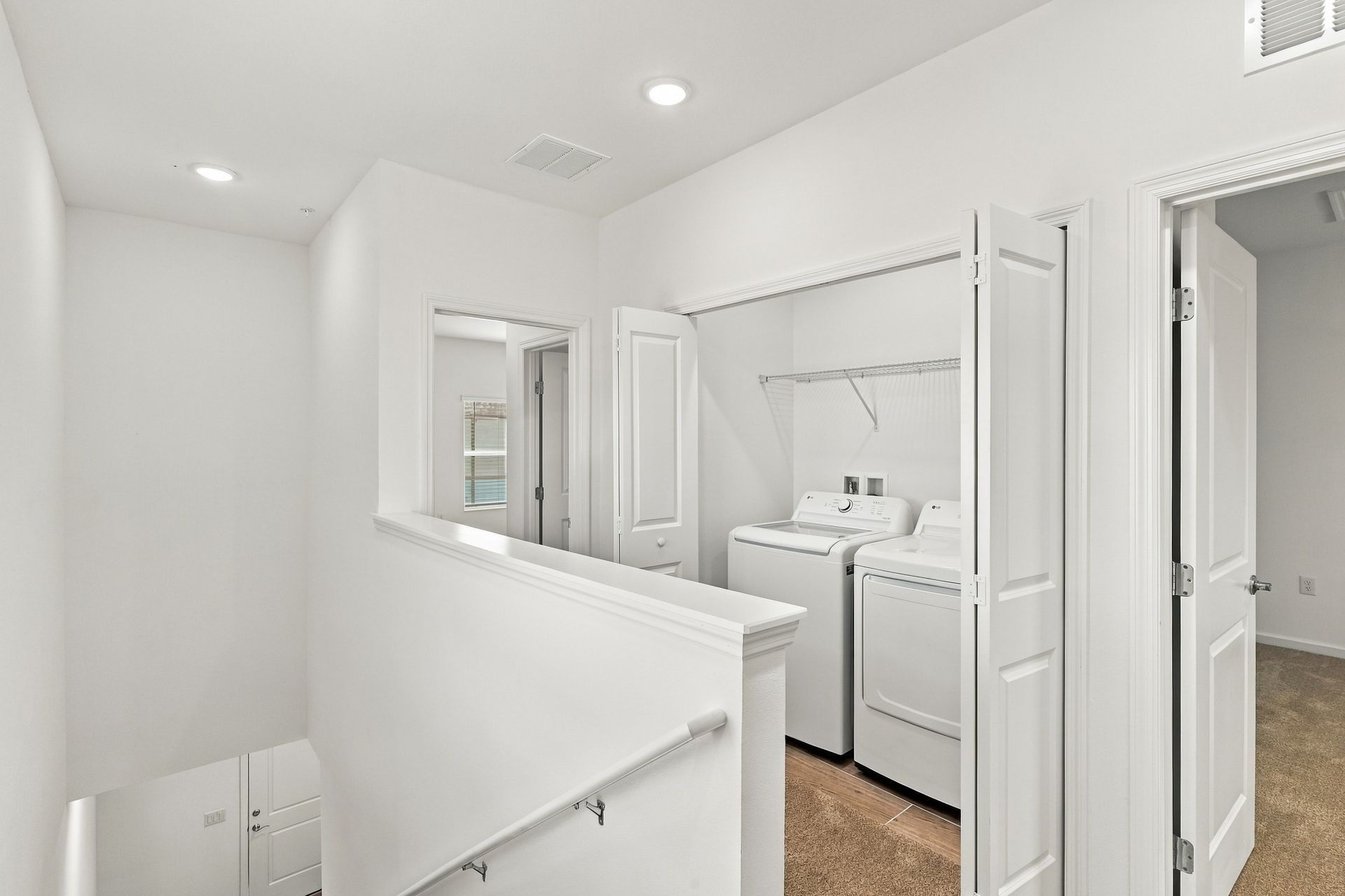 Bright white laundry room hallway with washer and dryer behind open closet doors