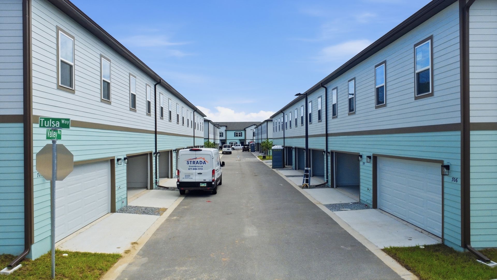 Two-story apartment walkway with garage doors, parked van, and teal siding under a blue sky