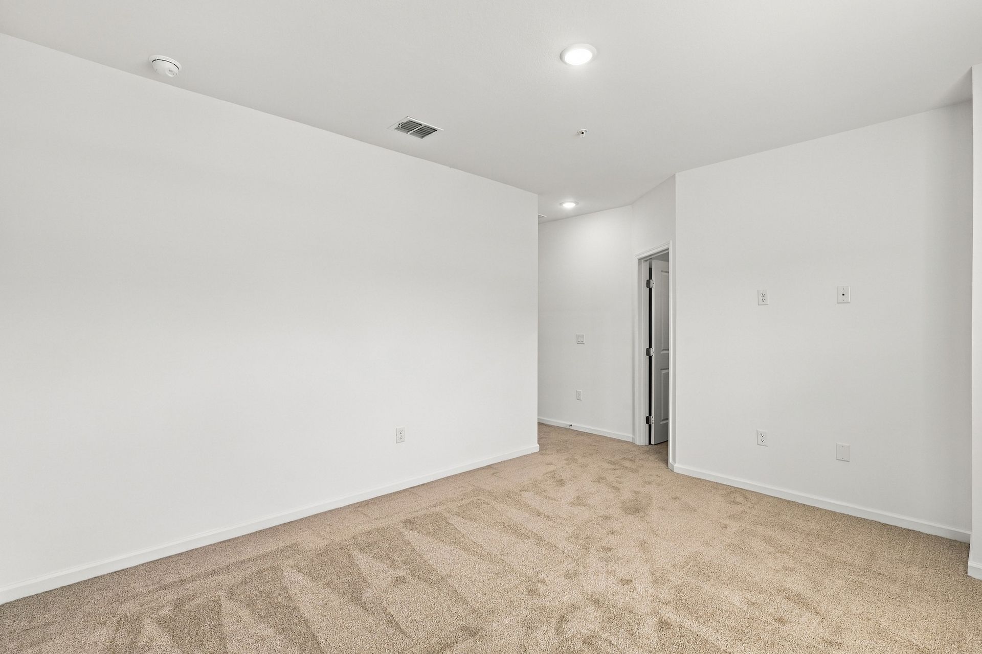 Empty white bedroom with beige carpet and recessed ceiling lights