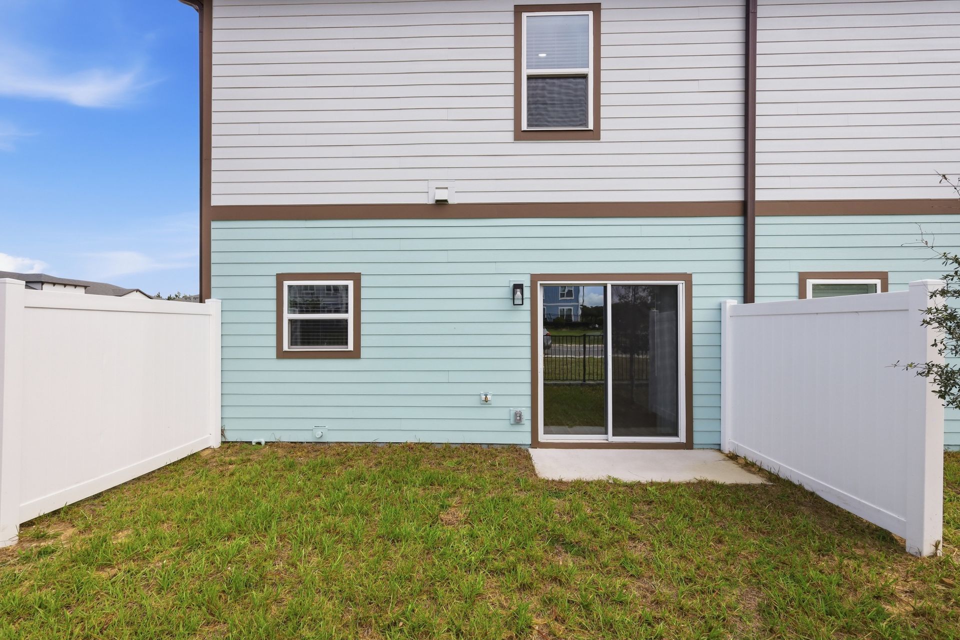 Small fenced backyard with sliding glass door on a two-story townhouse, grass lawn, and light blue siding.