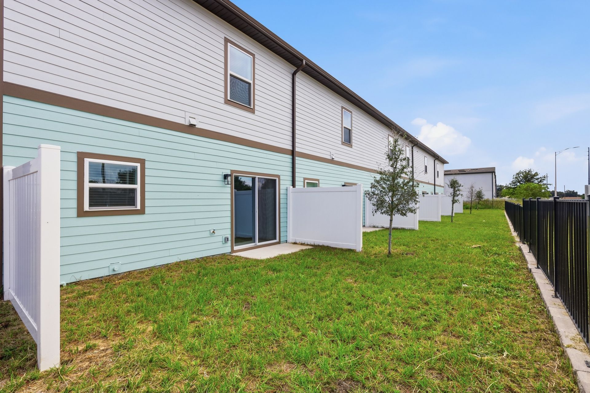 Backyard of a townhouse with a grassy lawn, sliding glass door, and a fence along the right side.