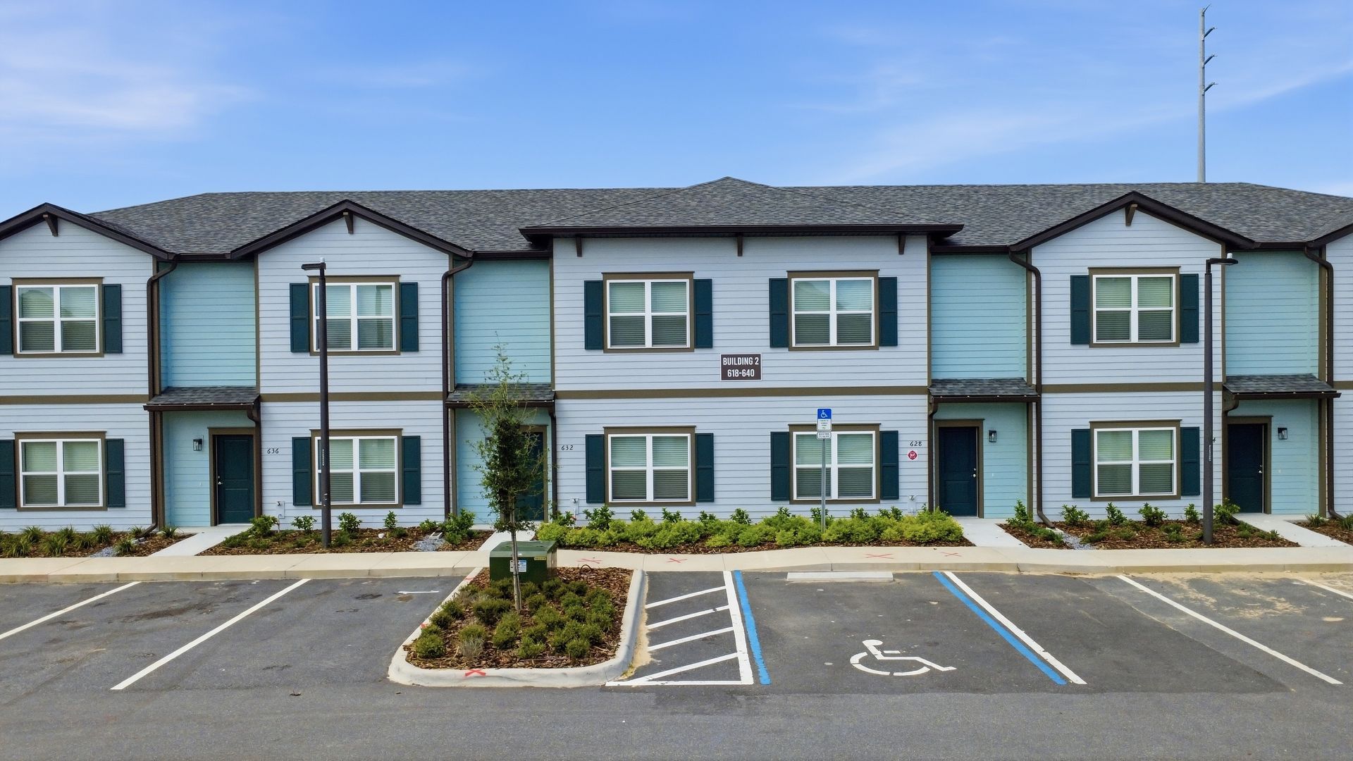 Exterior of a blue-gray apartment building with a parking lot and accessible spaces in front