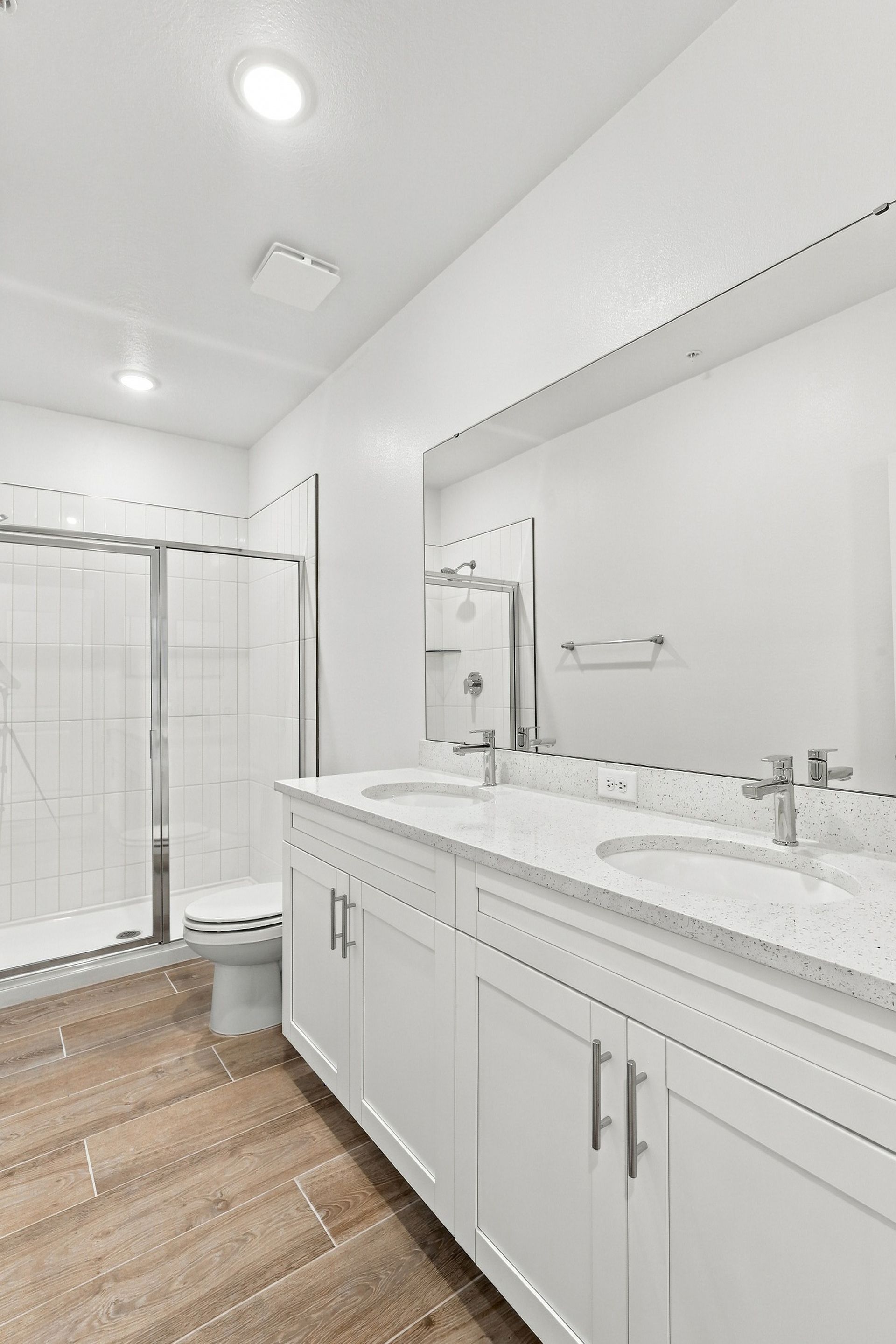 Bright modern bathroom with white vanity, large mirror, glass shower, and wood-look floor