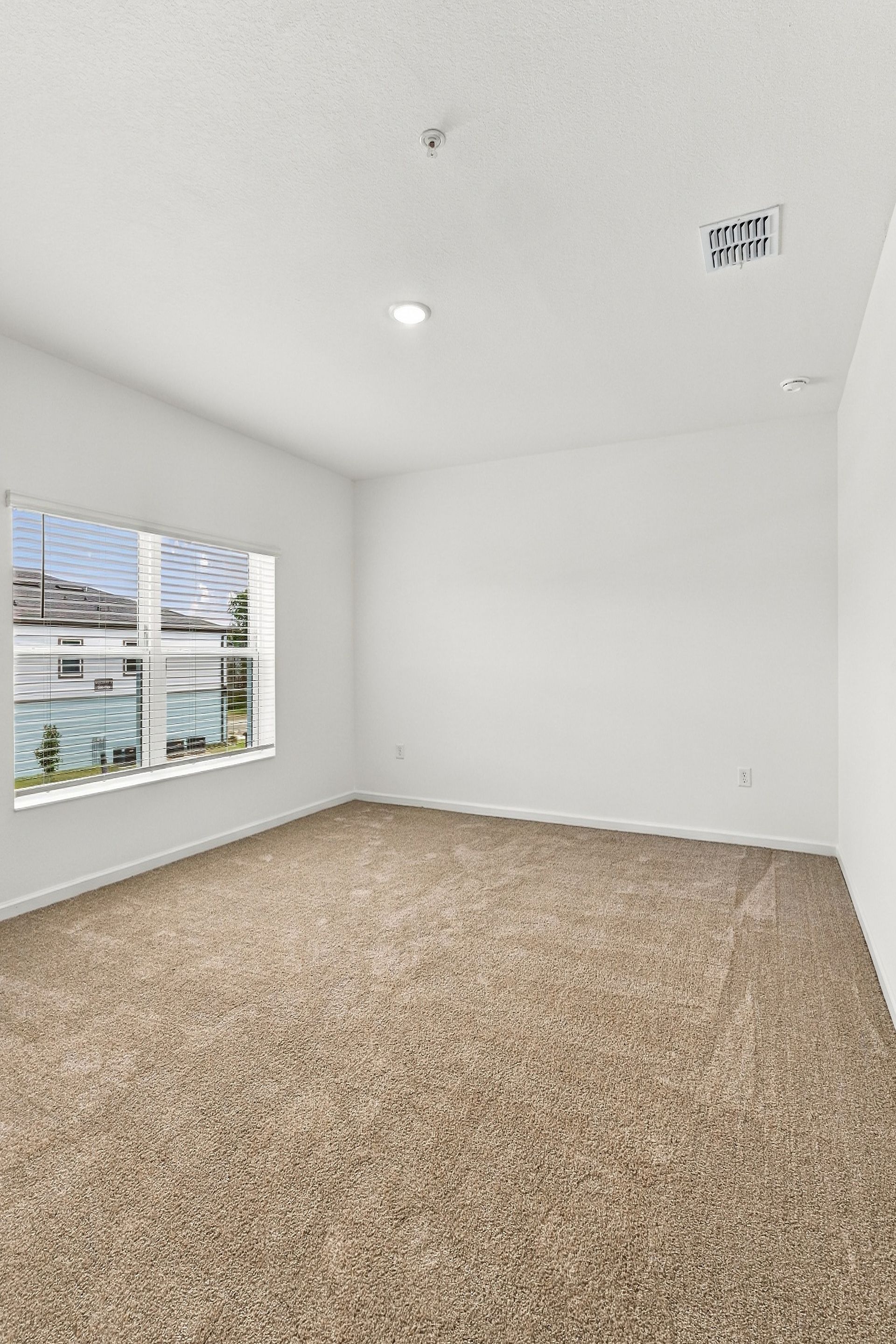 Empty white bedroom with beige carpet, window, and recessed ceiling light