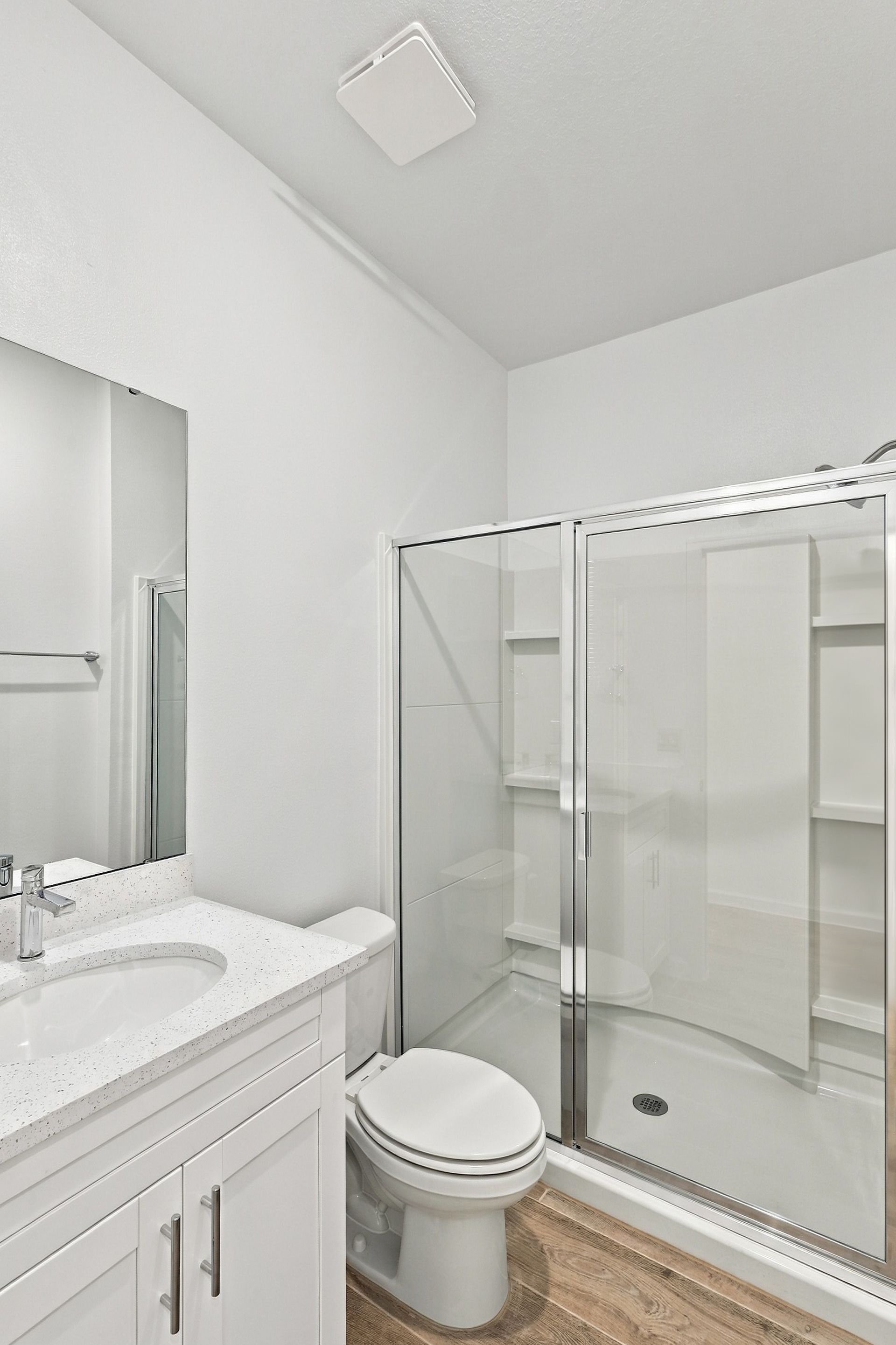 Small white bathroom with vanity, toilet, and glass-enclosed shower.