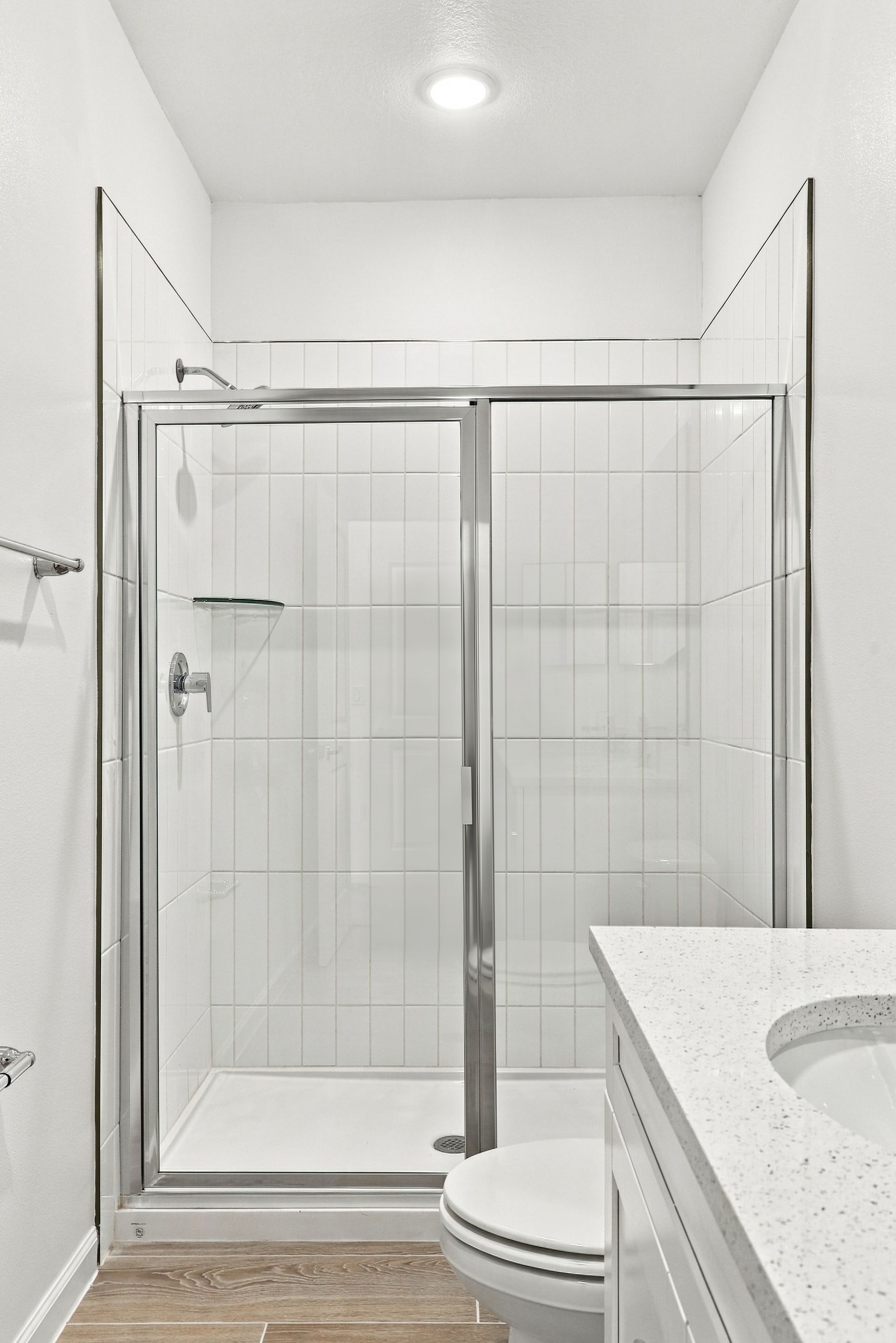 Small white bathroom with a glass shower, toilet, and vanity sink.