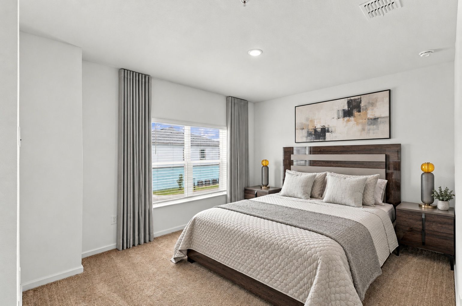 Bright bedroom with a neatly made bed, gray curtains, nightstands, and a large window with a water view.