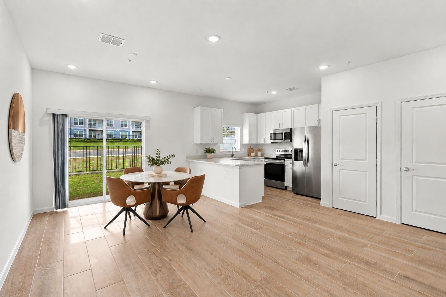 Bright open-plan kitchen and dining area with white cabinets, wood floors, and sliding glass doors to a backyard.