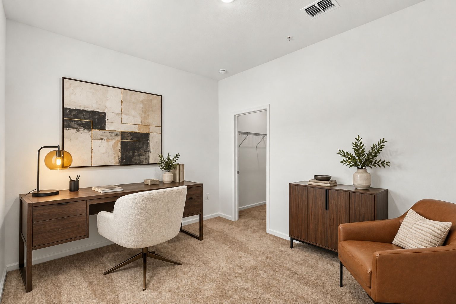 Minimal home office with desk, chair, wall art, side cabinet, and tan armchair on beige carpet