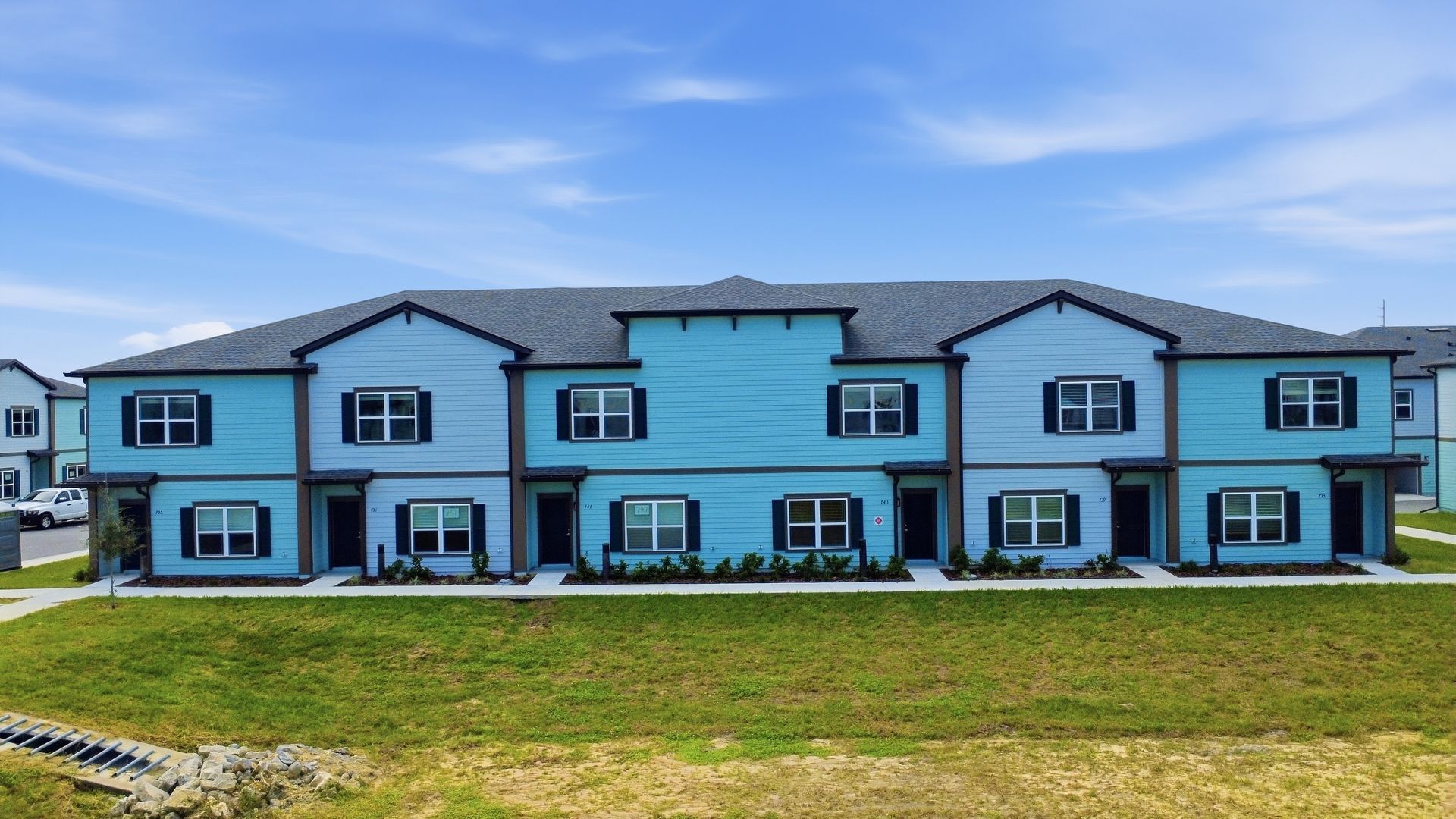 Blue two-story apartment building with multiple doors and windows on a grassy lawn under a clear sky
