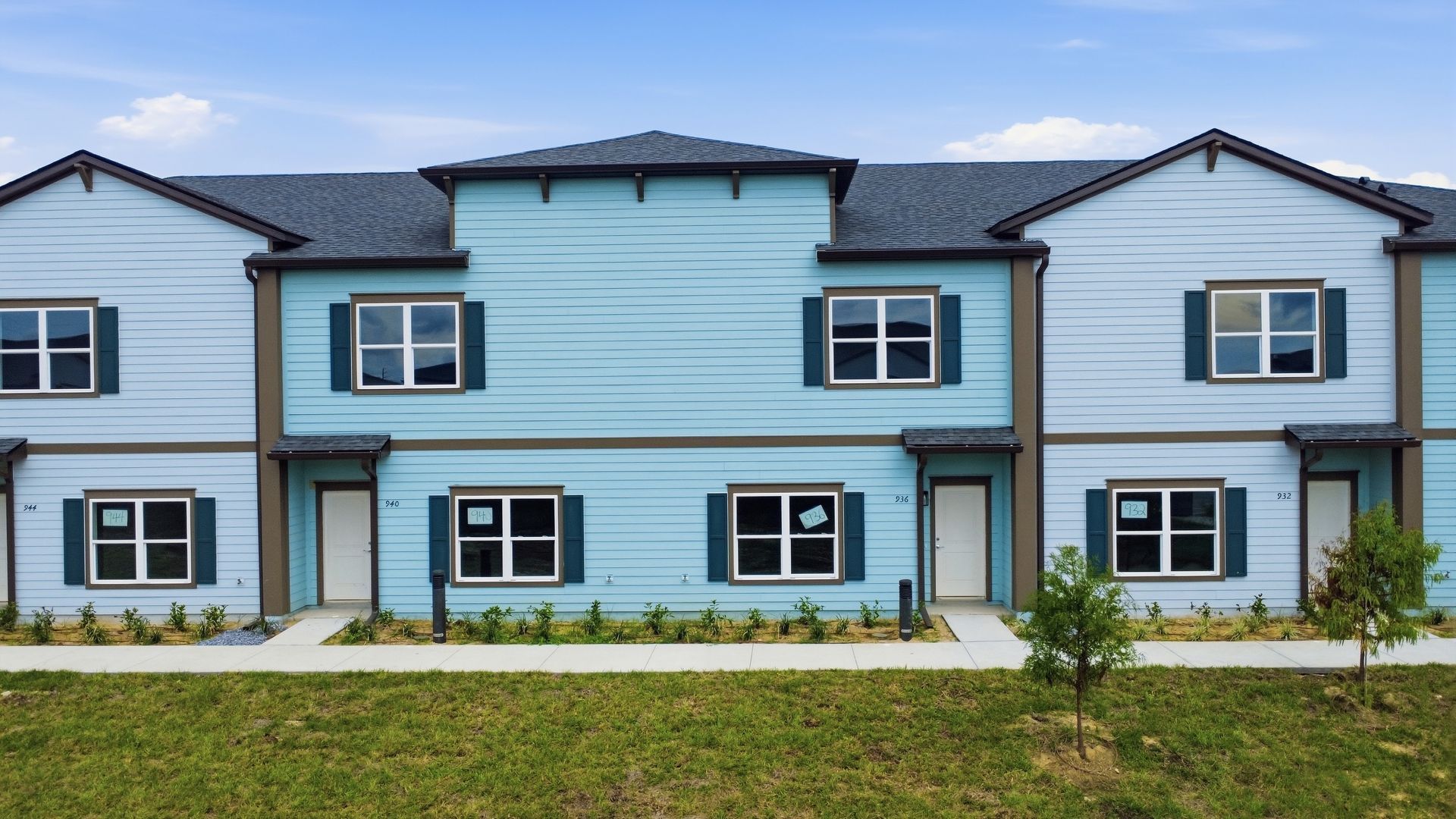 Row of modern blue townhouses with white trim and small front lawns under a clear sky