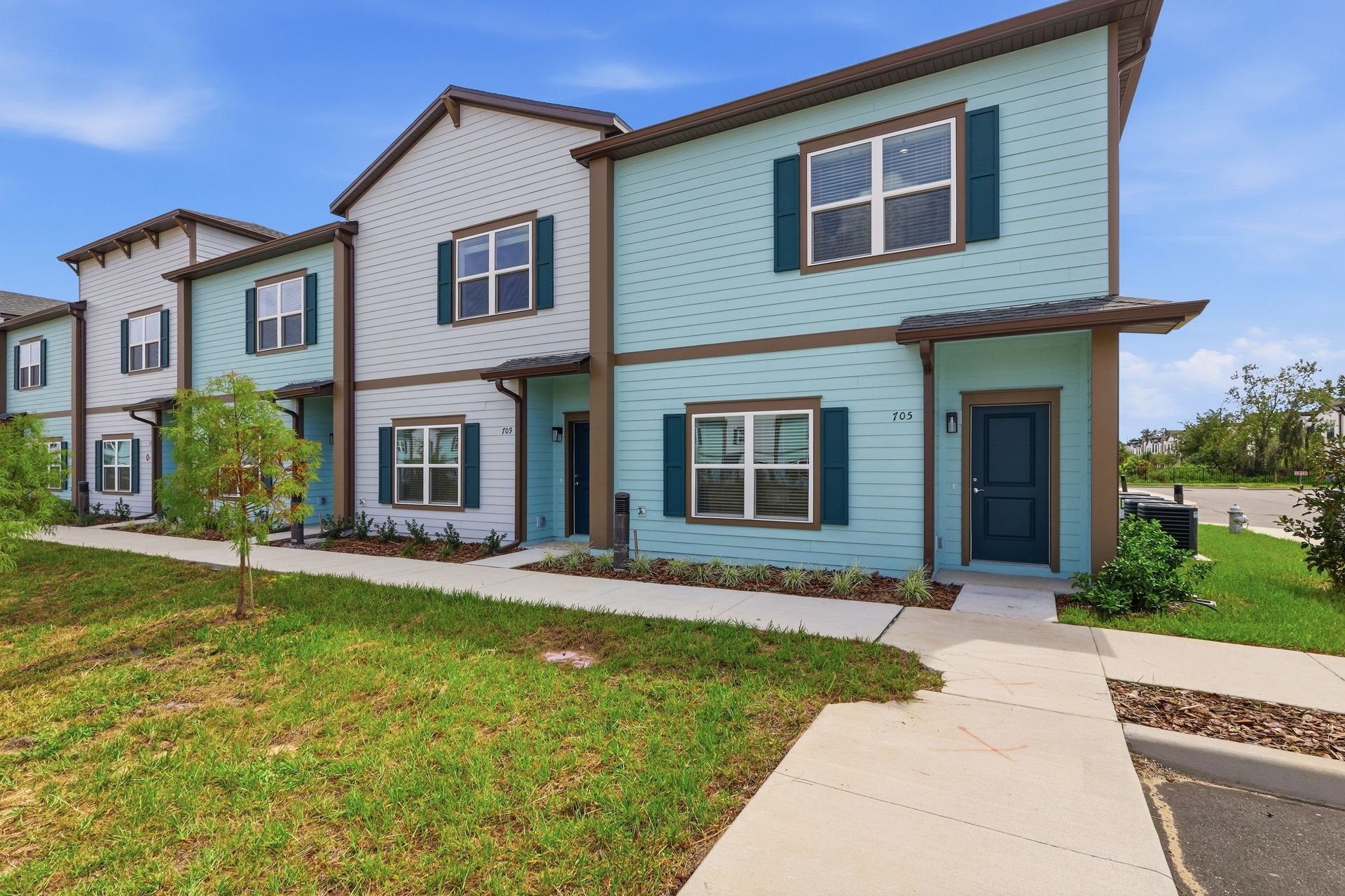 Row of modern townhomes with light blue siding, white trim, and a sidewalk in front