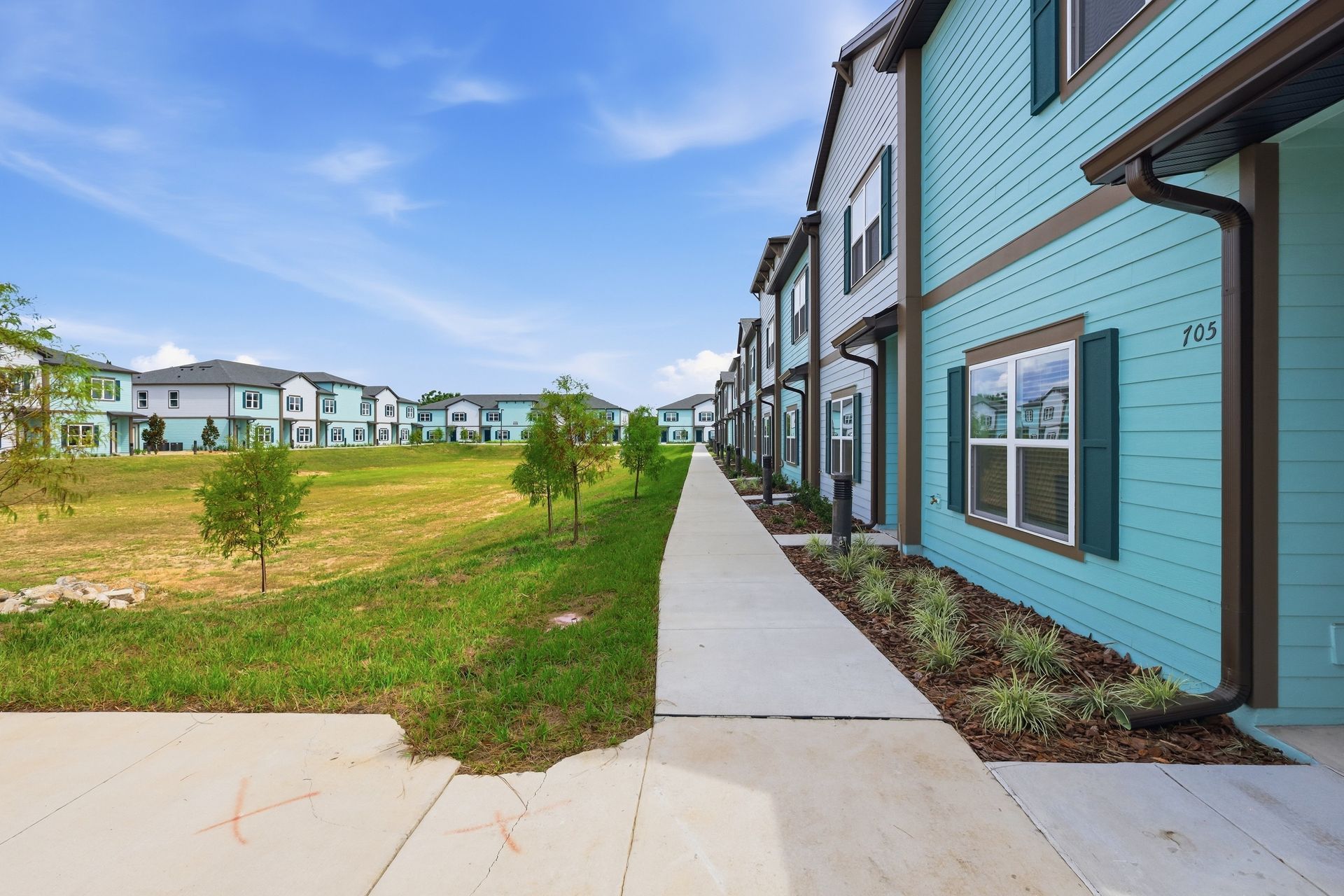 Apartment buildings beside a sidewalk and grassy lot under a blue sky