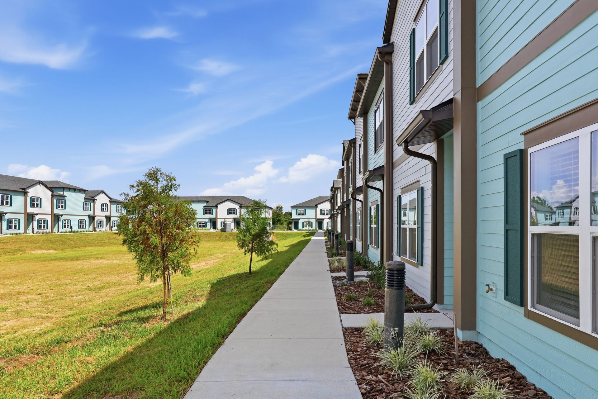 Apartment buildings beside a sidewalk and grassy courtyard on a sunny day