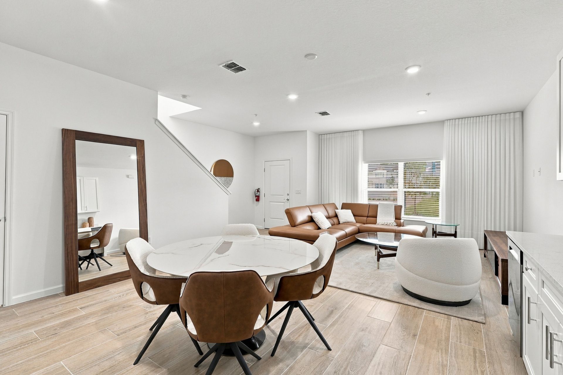 Bright modern living room with white walls, wood floors, and tan chairs around a round table