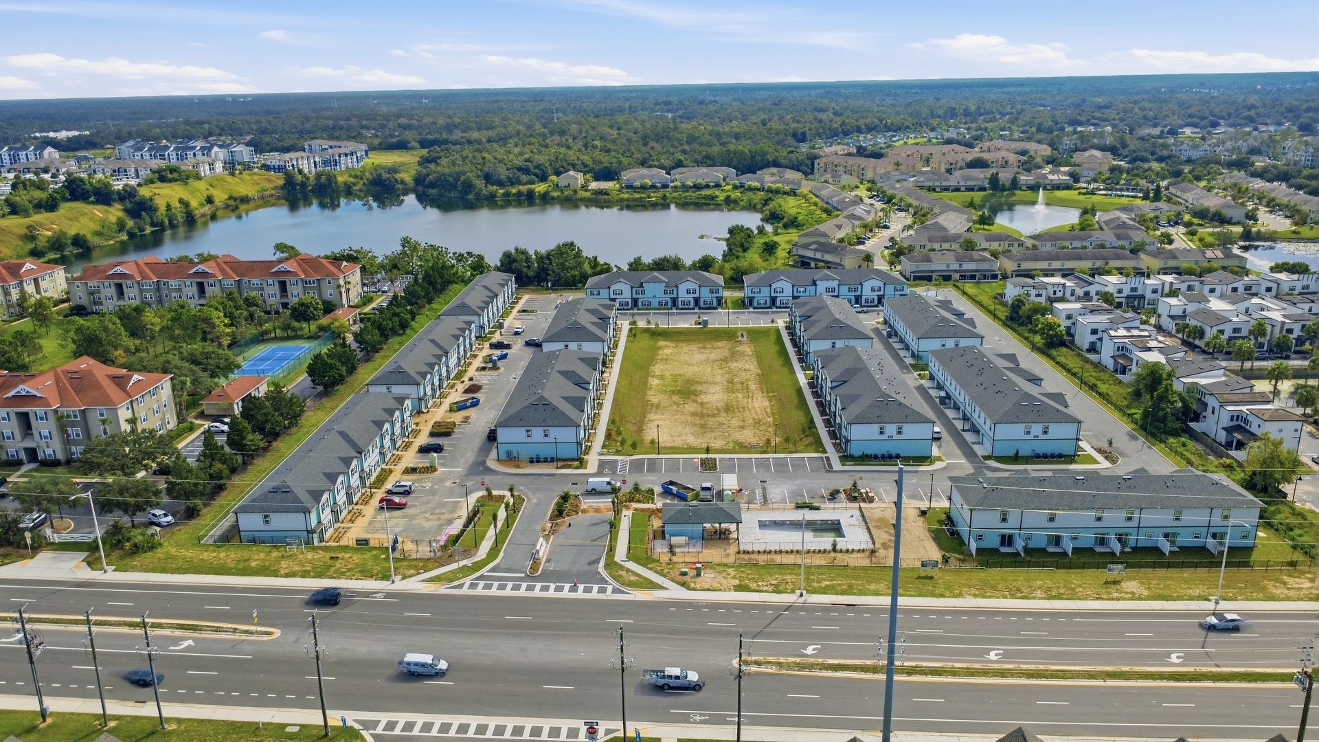 Aerial view of a suburban shopping center with parking lots, roads, and surrounding trees and homes.