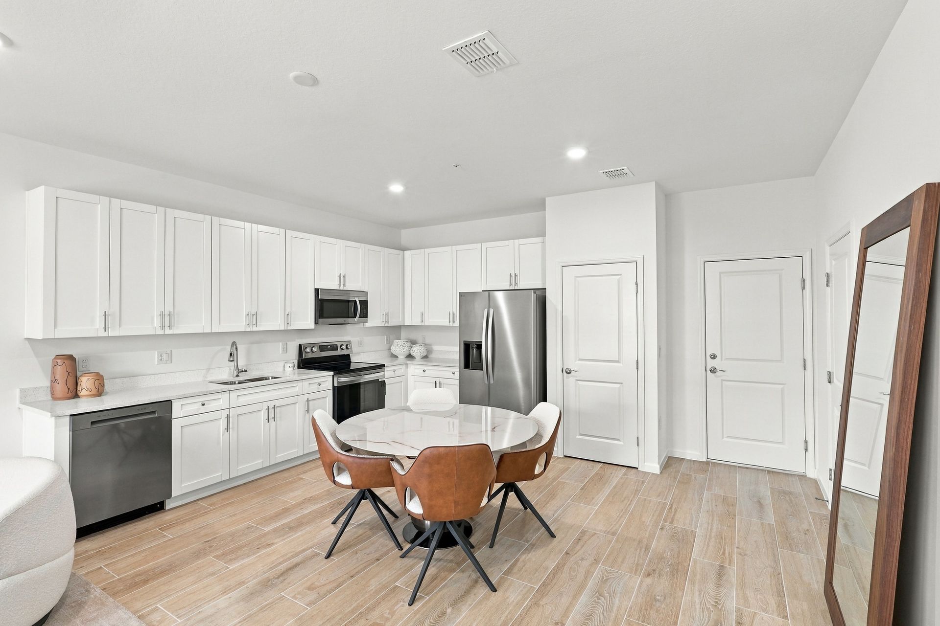Bright white kitchen and dining area with wood floors, stainless appliances, and a round table with chairs