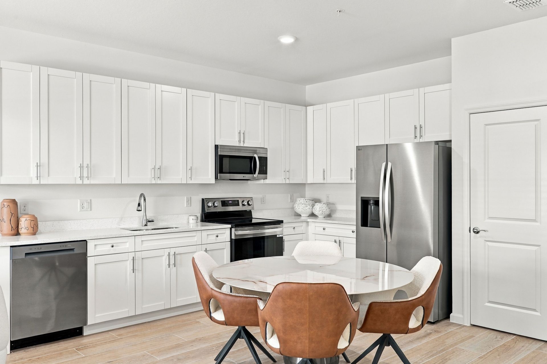 Bright white kitchen with stainless steel appliances and a round dining table with brown chairs