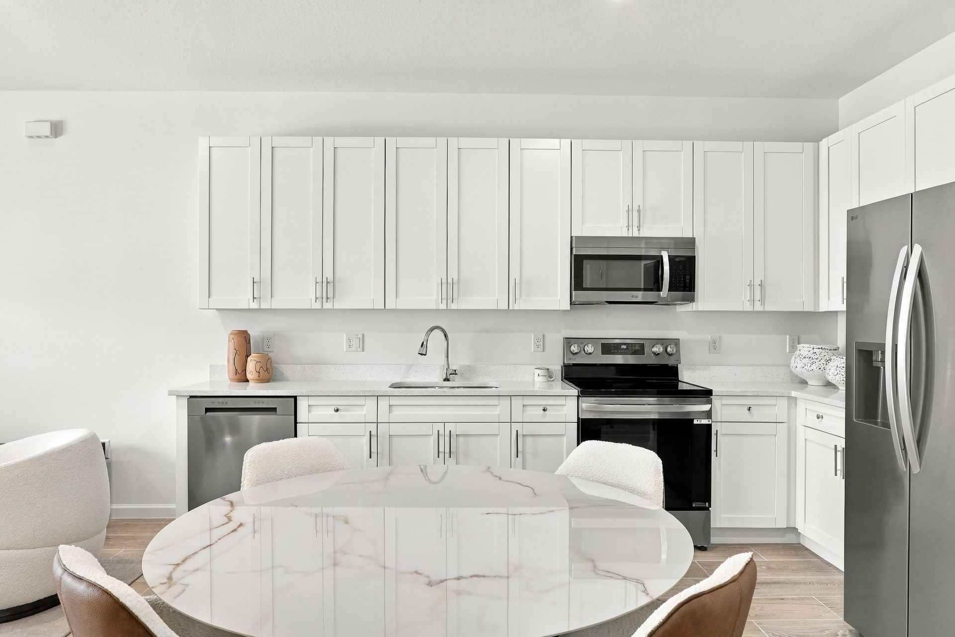 Bright white kitchen with stainless appliances, marble table, and white cabinets
