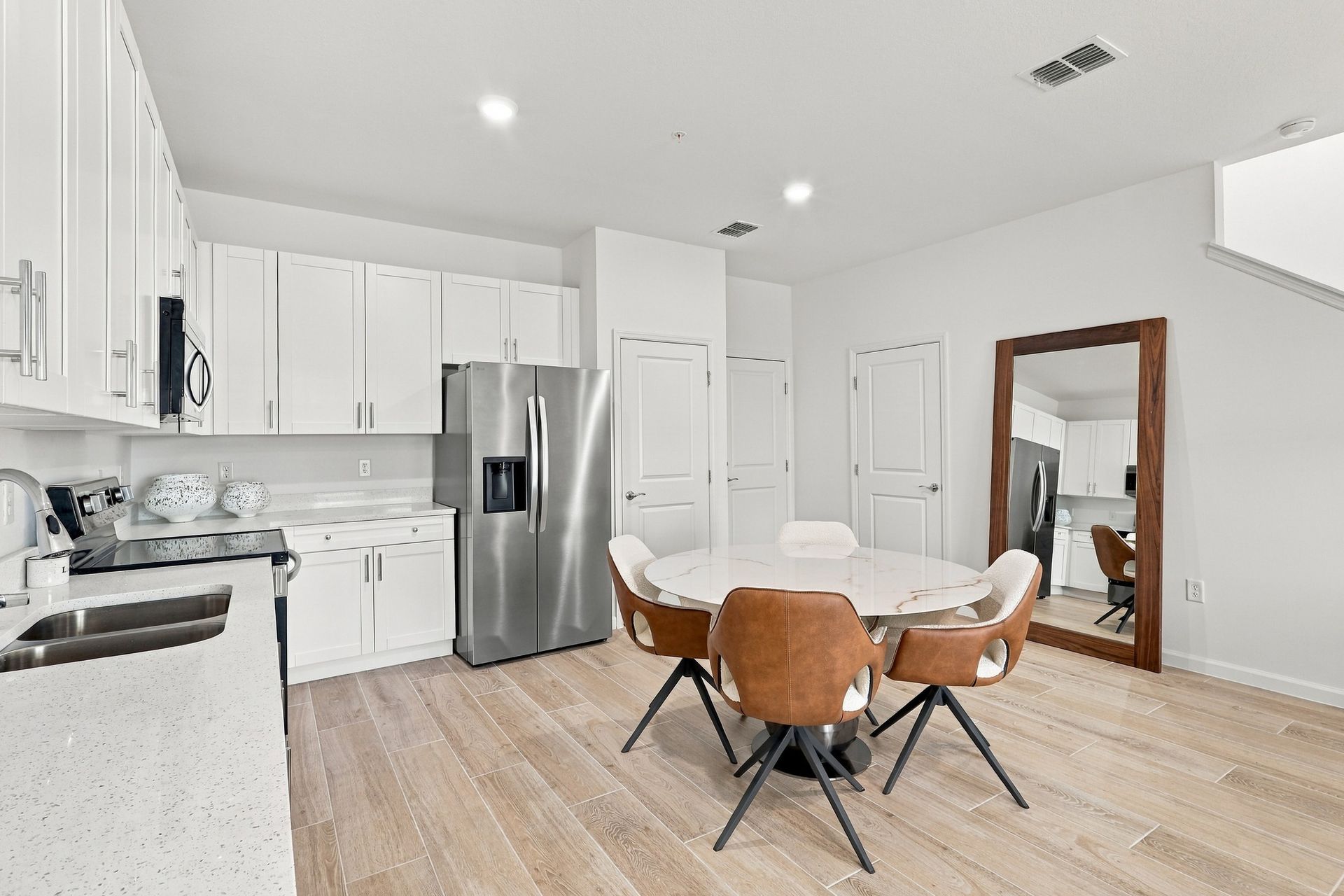 Bright white kitchen and dining area with stainless steel fridge, round table, and wood floors