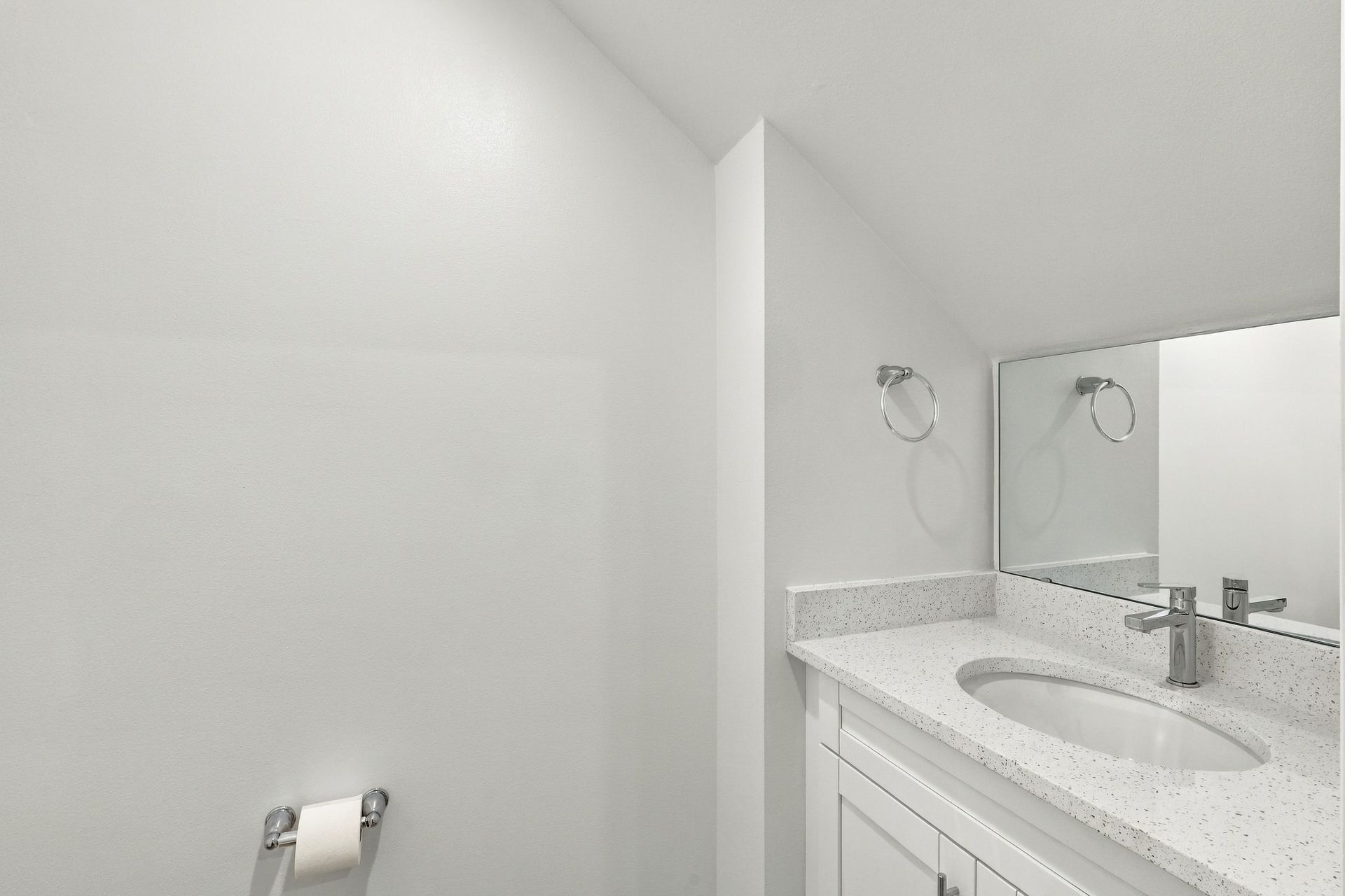 Bright white bathroom with sink, mirror, towel ring, and toilet paper holder