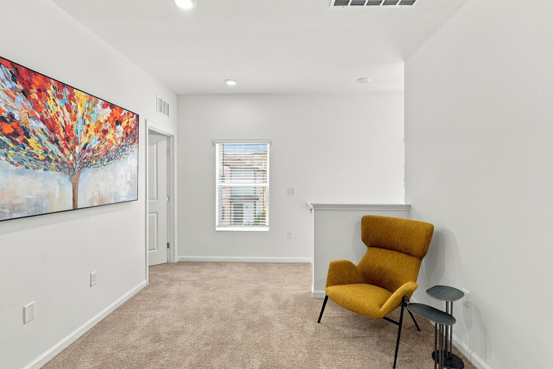 Bright white room with colorful wall art, mustard chair, small side table, and window.