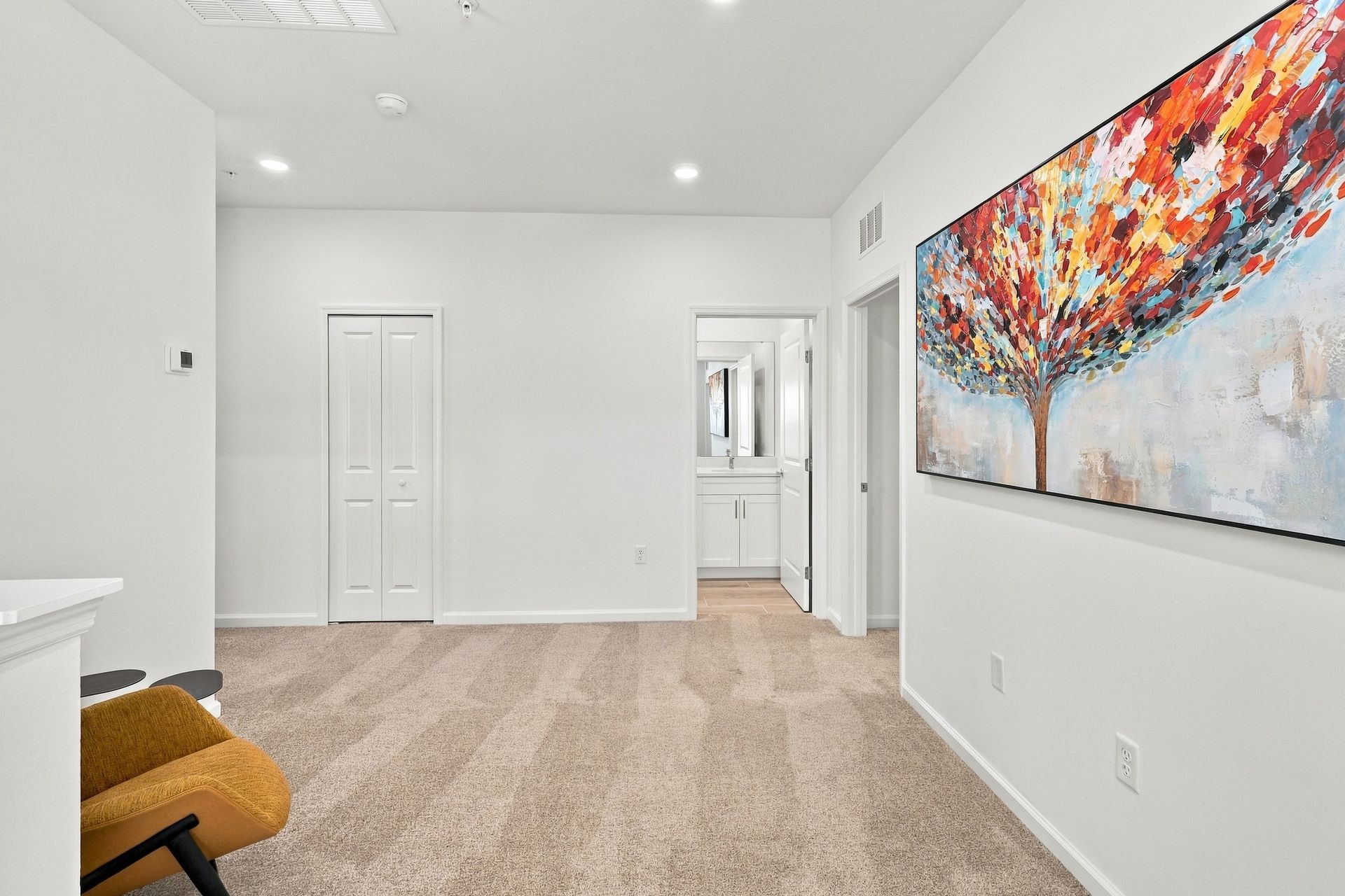 Bright white bedroom with beige carpet, abstract wall art, and a small bench near mirrored closet doors.