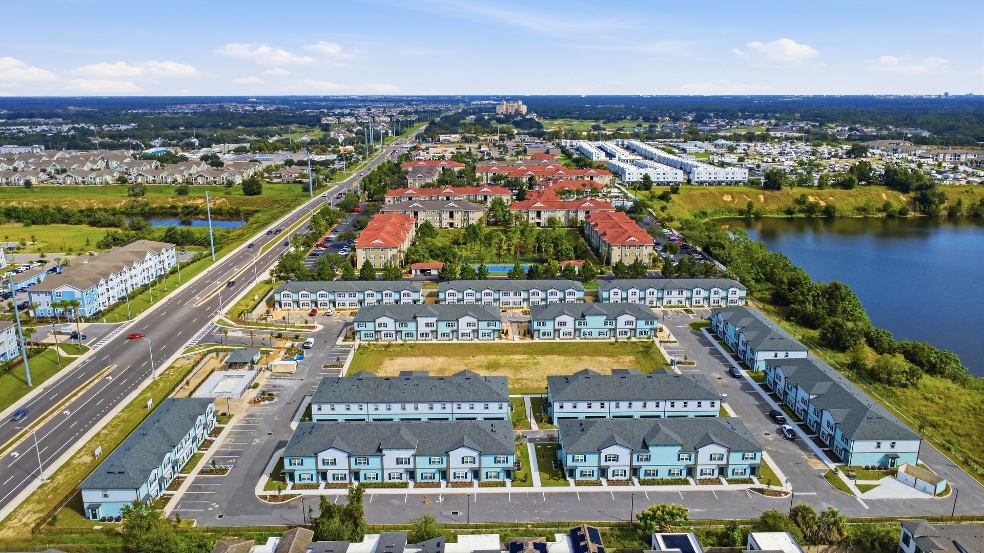 Aerial view of a suburban neighborhood with rows of townhouses, roads, and water channels under a clear sky