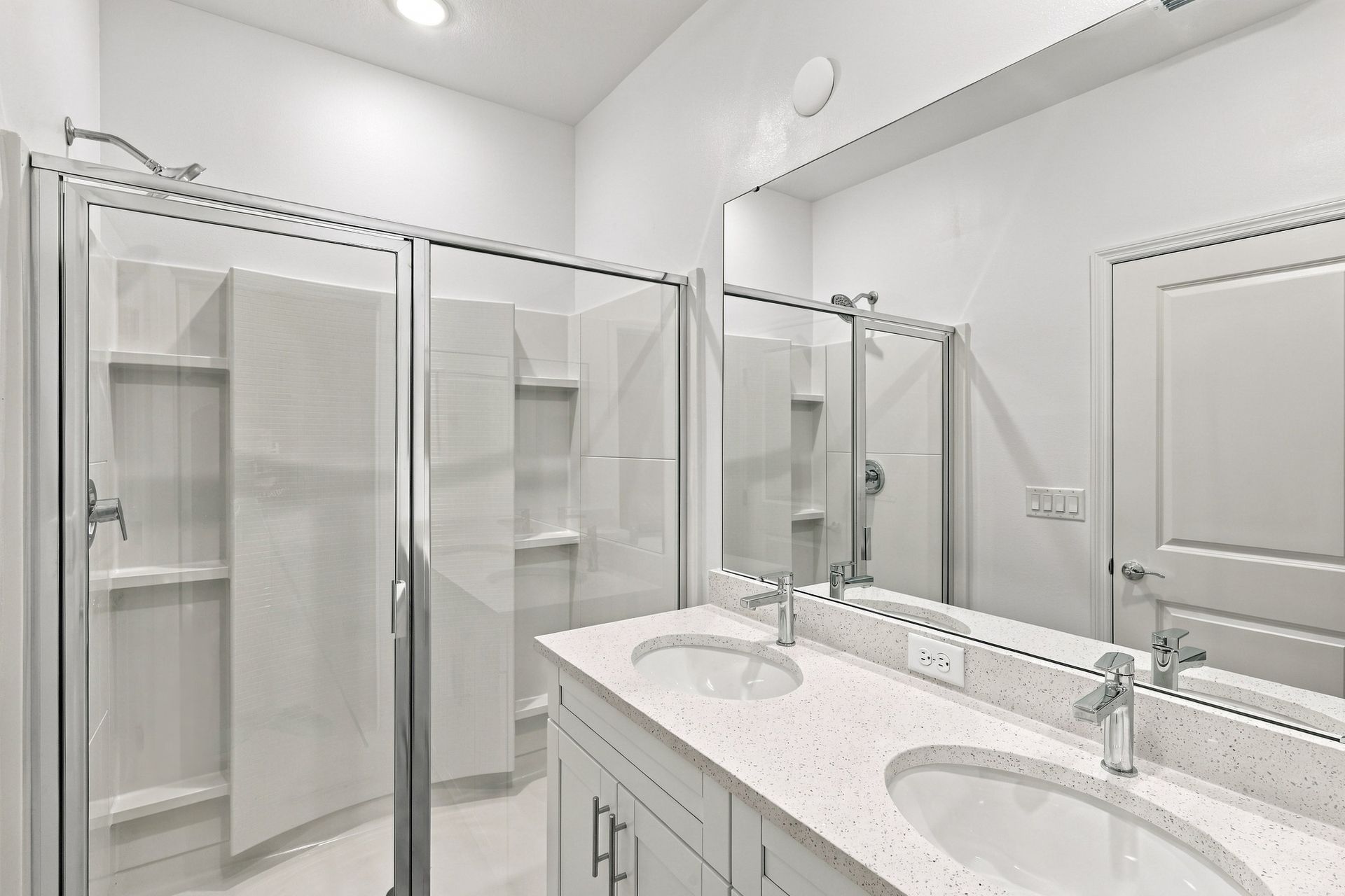 Bright white bathroom with dual sinks, large mirror, and glass shower and closet doors