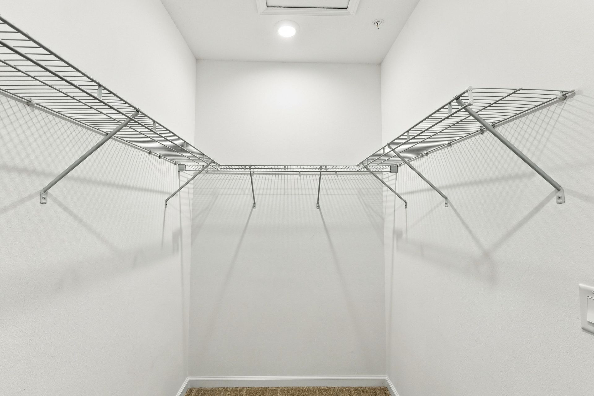 Empty white walk-in closet with wire shelving on both sides and a light overhead