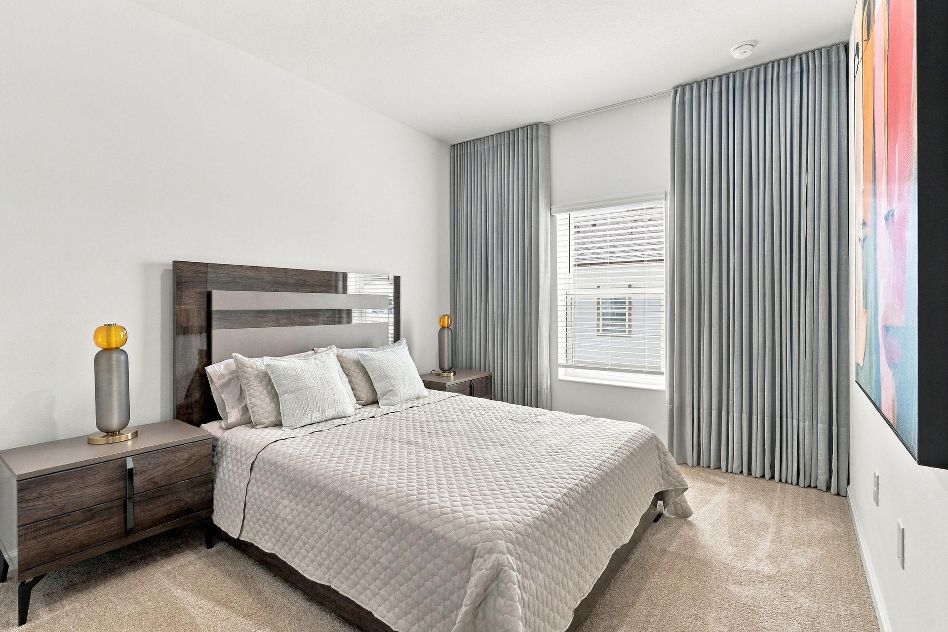 Bright bedroom with a gray bed, striped curtains, nightstands, and soft natural light