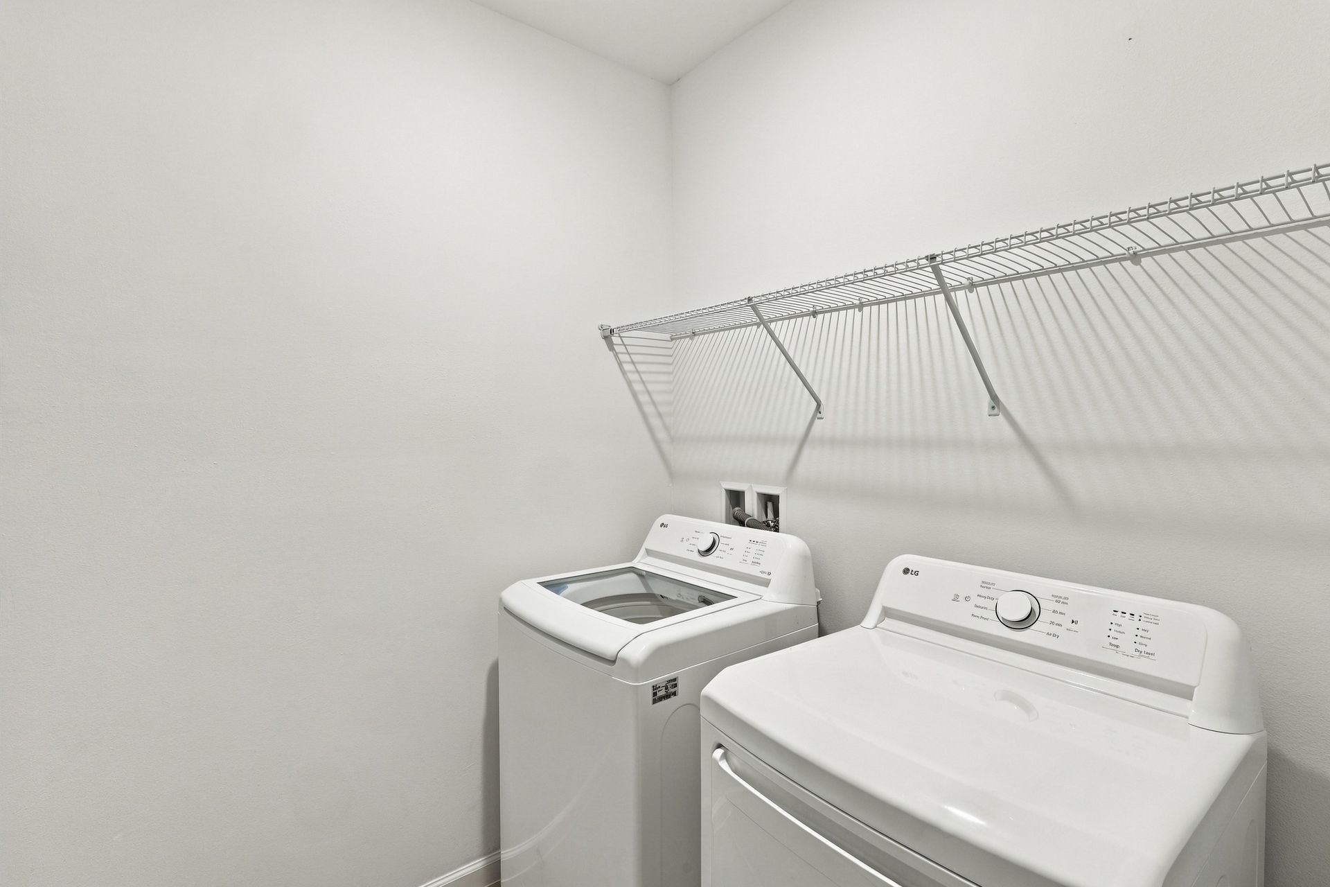 Small laundry room with a washer, dryer, and wire shelf on a white wall.