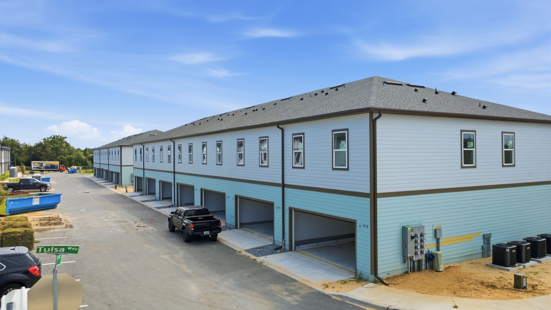 Row of gray-blue apartment buildings with covered parking and a black car in a lot