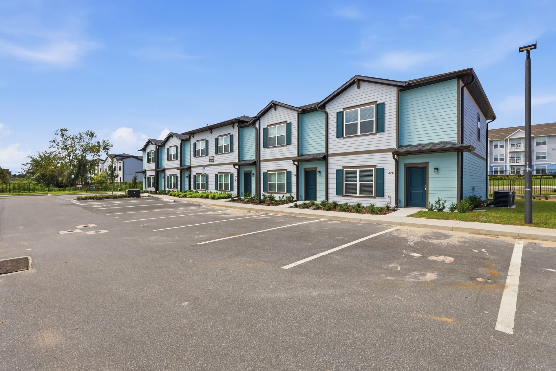 Row of blue townhouses beside an empty parking lot under a clear sky