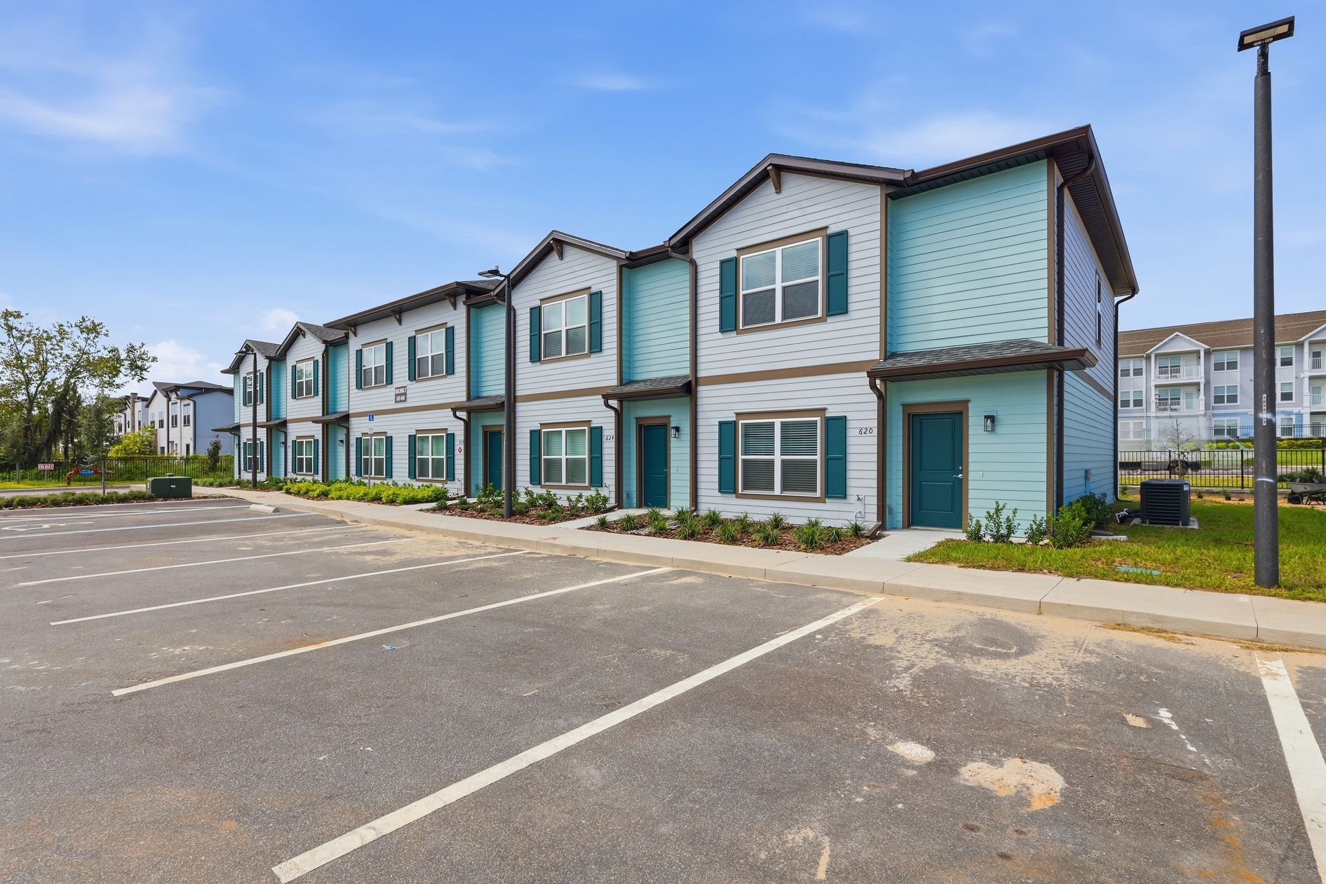 Blue apartment buildings beside an empty parking lot on a clear day