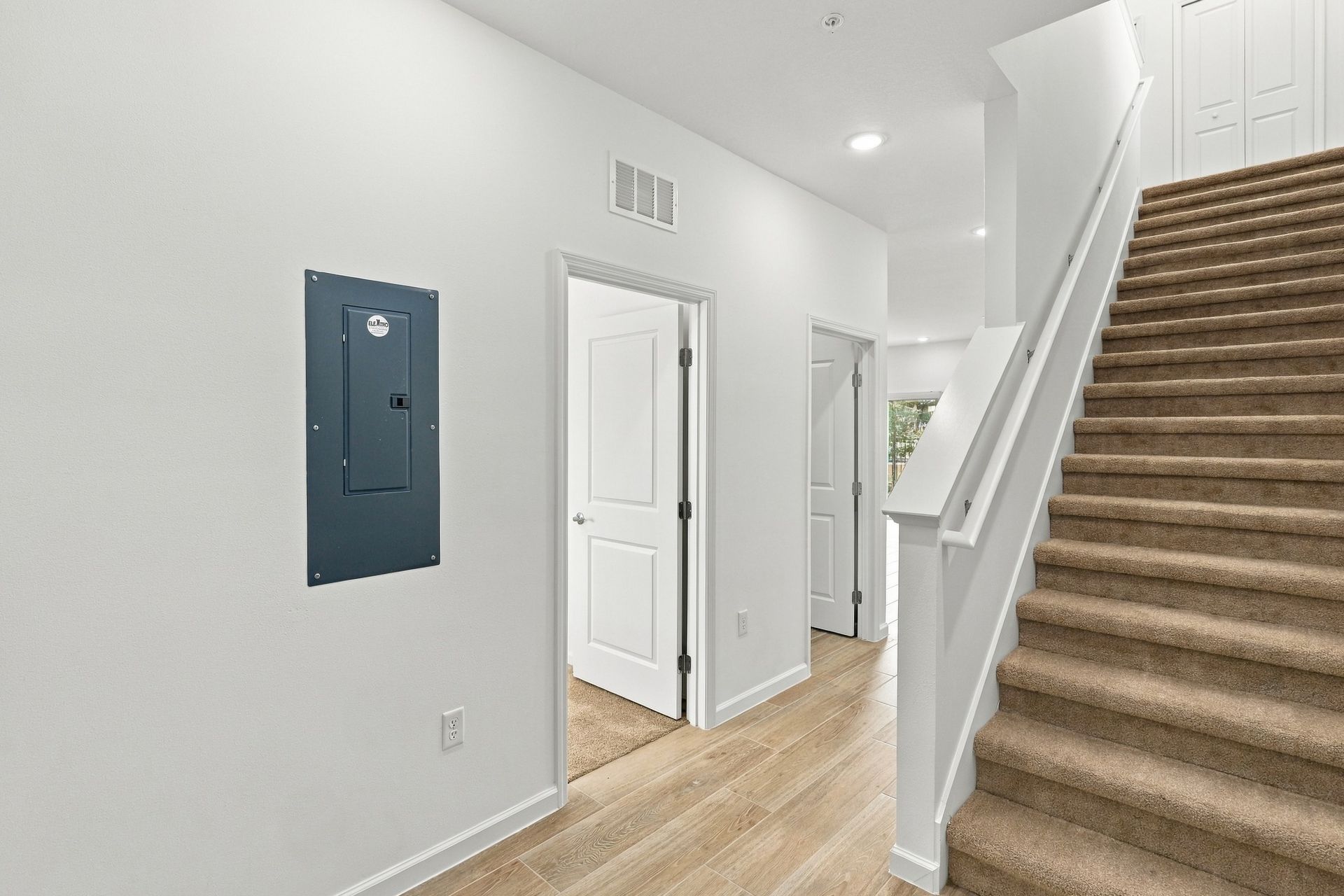 Bright entry hall with staircase, white walls, wood floor, and blue electrical panel on left wall