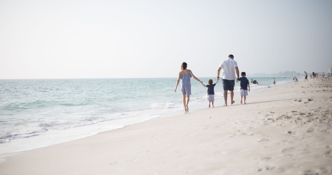 Family walking along a sandy beach beside the ocean on a bright day