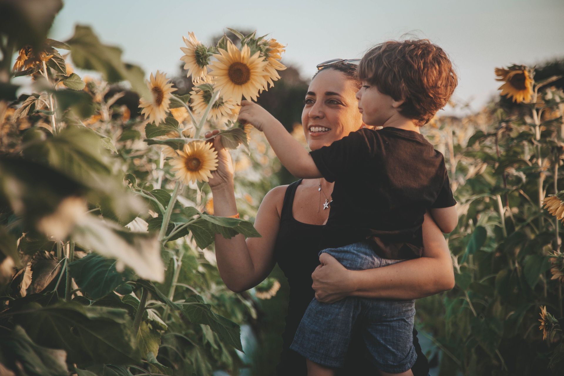 Woman holding a child in a sunflower field, pointing at the flowers.