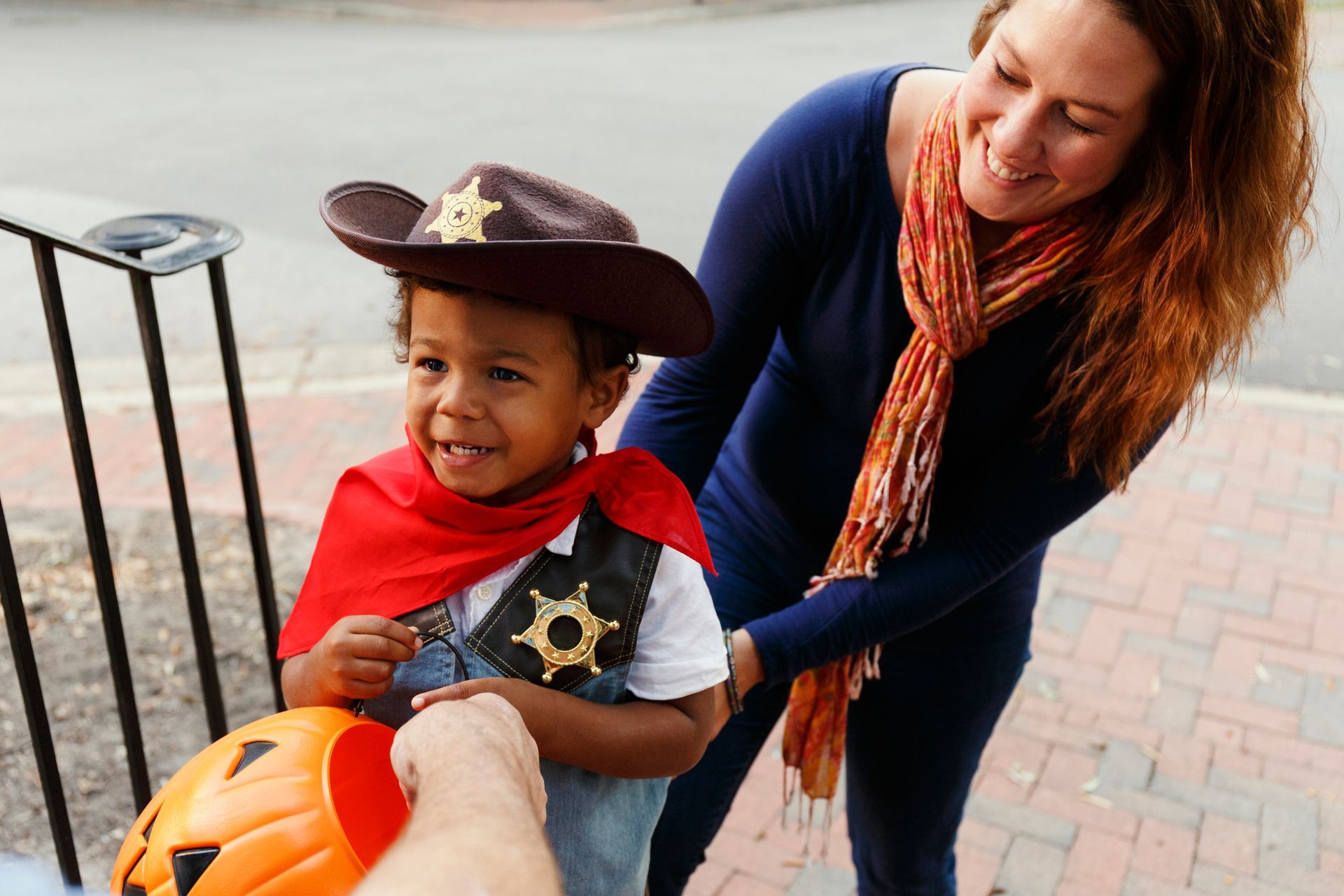 Child in cowboy costume receives candy from person, smiles, with adult next to them.